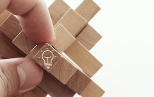 close up of hand showing illuminated light bulb icon on a wooden block puzzle as innovation concept