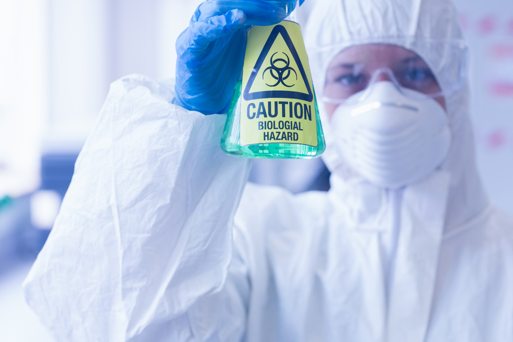 Close-up of a scientist in protective suit with hazardous blue chemical in flask at the laboratory Close-up of a scientist in protective suit with hazardous blue chemical in flask at the laboratory